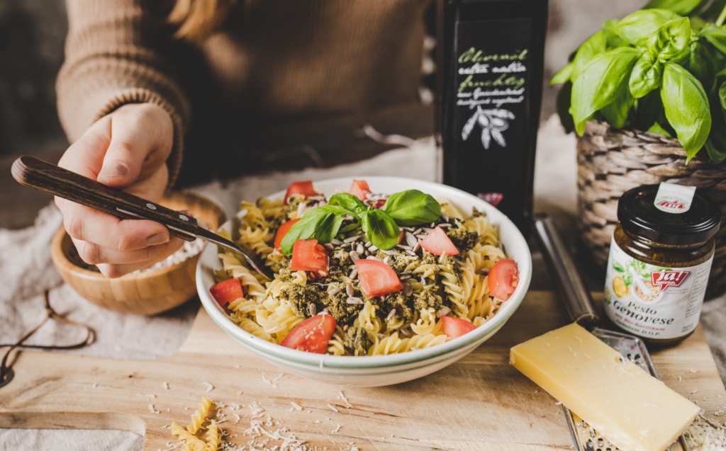 Ein Teller Spirelli mit Ja! Natürlich Bio-Pesto, Tomaten und eine Flasche Olivenöl daneben.
