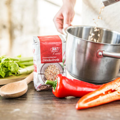 Eine Packung Ja! Natürlich Bio-Dinkelreis, ein Topf und rote Spitzpaprika.