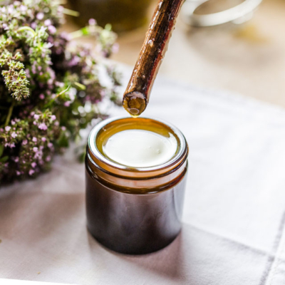 Jemand hält einen Stock über ein Glas mit Bio-Thymian-Balsam.