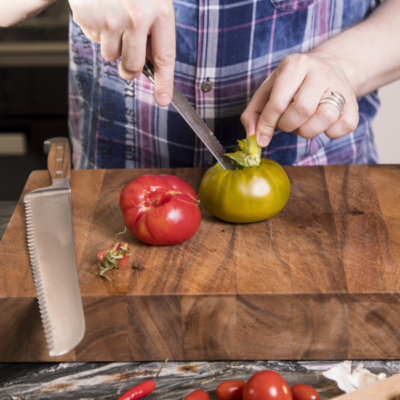 Jemand schneidet Bio-Paradeiser auf einem Schneidebrett.
