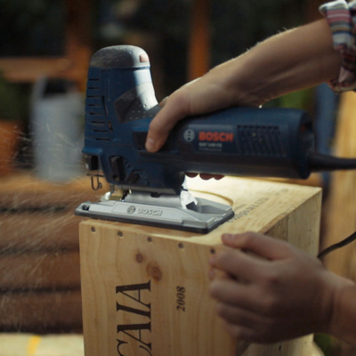 Jemand schneidet eine Weinkiste mit einer Stichsäge.