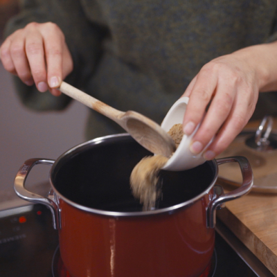 Jemand gibt Bio-Rohrohrzucker in einen Topf.