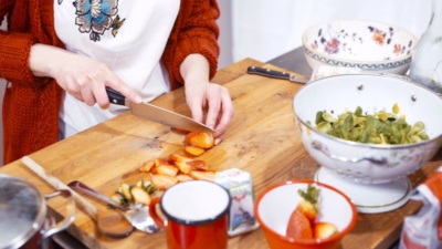 Jemand schneidet Bio-Erdbeeren, daneben steht ein Becher Ja! Natürlich Bio-Ziegenfrischkäse.