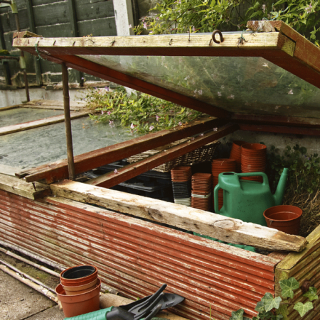 Geöffnetes Frühbeet mit Töpfen und Gießkannen.