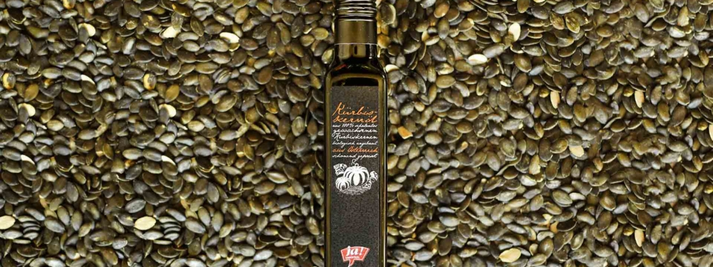Eine Flasche Ja! Natürlich Bio-Kürbiskernöl, darunter Kürbiskerne.