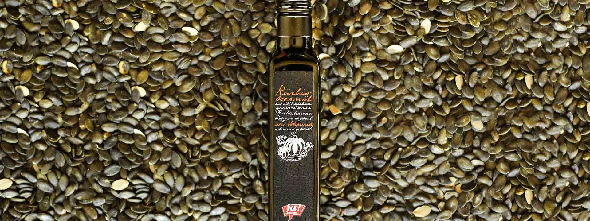 Eine Flasche Ja! Natürlich Bio-Kürbiskernöl, darunter Kürbiskerne.