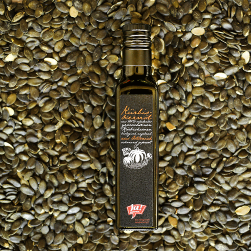Eine Flasche Ja! Natürlich Bio-Kürbiskernöl, darunter Kürbiskerne.