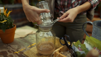 Nahaufnahme von Händen, die durch einen Sieb in ein Gefäß gießen.