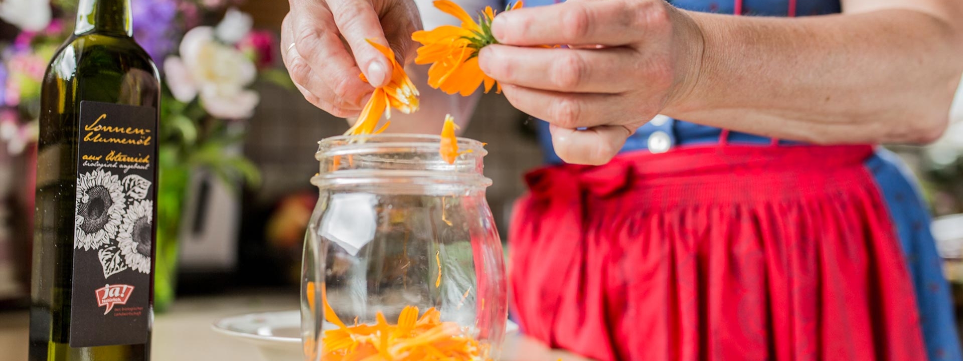 Jemand zerpflückt Ringelblumen, daneben steht eine Flasche Ja! Natürlich Bio-Sonnenblumenöl.