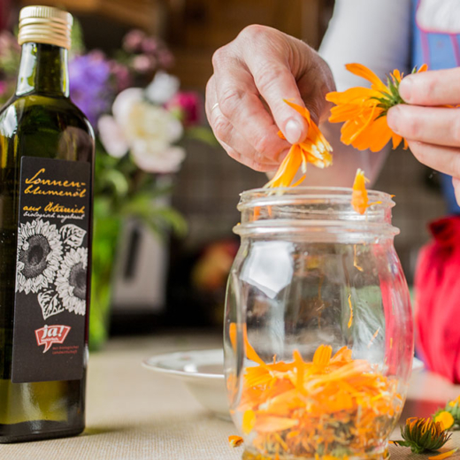 Jemand zerpflückt Ringelblumen, daneben steht eine Flasche Ja! Natürlich Bio-Sonnenblumenöl.