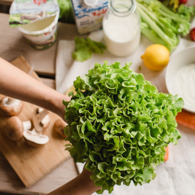 Jemand hält Blattsalat ins Bild, im Hintergrund sieht man Ja! Natürlich Milchprodukte.