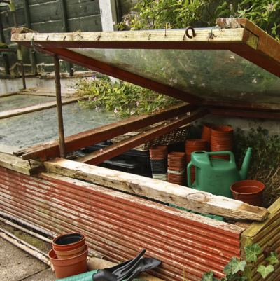Ein geöffnetes Frühbeet mit Töpfen und Gießkannen drin.