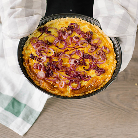 Jemand hält eine Bio-Zwiebelquiche mit Ofenhandschuhen.