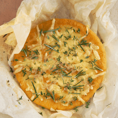 Eine gebackene Alpenpizzelette auf einem Backpapier mit Bio-Bergkäse und Kräutern.