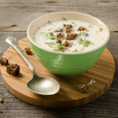 Eine Schüssel mit Bauernrahmsuppe und Bio-Brotkrumen auf einem runden Holztablett.