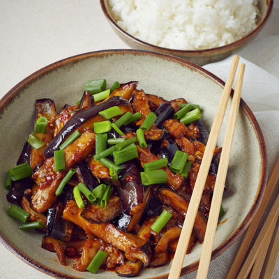 Veganes Melanzani-Gericht in einer Bowl, daneben eine kleine Schüssel Bio-Reis.