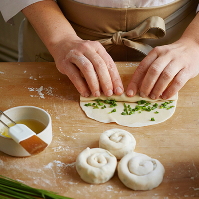 Jemand rollt einen Teig mit Bio-Schnittlauch zu kleinen Teigschnecken.