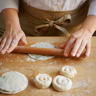 Jemand walkt mit einem Nudelholz einen Teig aus.