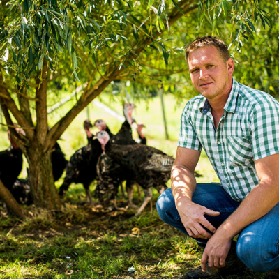 Bio-Bauer Hans-Peter Bramauer kniend vor Freiland-Puten.