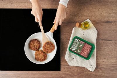 Jemand brät faschierte Laibchen in einer Pfanne, daneben eine Packung Ja! Natürlich Bio-Faschiertes.