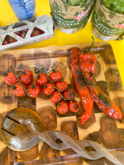 Geröstete Bio-Paprika und Tomaten auf einem Schneidebrett.