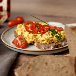 Ein Teller mit zwei Bio-Eierspeisbrote mit Paradeisern und Paprikascheiben.