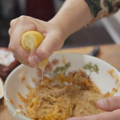 Jemand presst eine Bio-Zitrone in einen Teig.