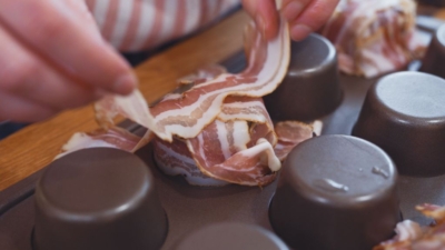 Jemand belegt umgedrehte Muffinformen mit Bio-Speck.