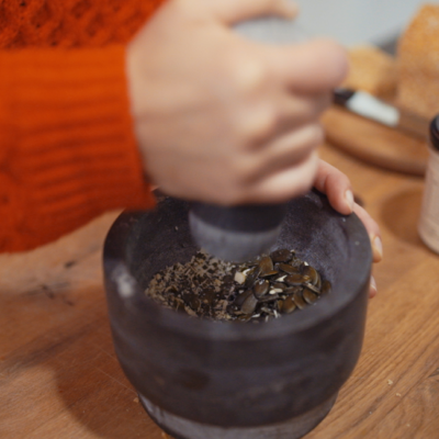 Jemand zerstampft Bio-Kürbiskerne mit einem Mörser.