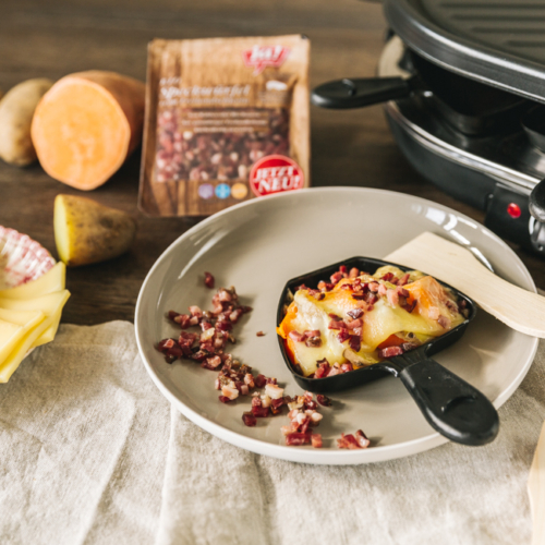 Raclette-Pfännchen mit Käse und Ja! Natürlich Bio-Speckwürfeln.