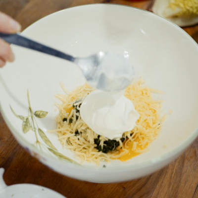 Jemand vermengt Bio-Mehl, Blattspinat, Eier und Käse in einer Schale.