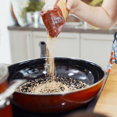 Jemand schüttet Bio-Sesam in eine Pfanne.