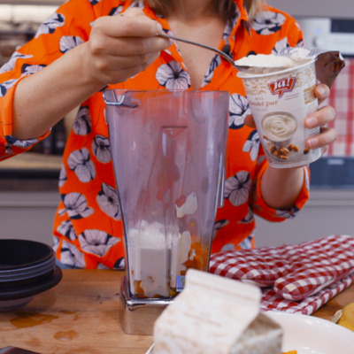 Jemand gibt einen Löffel Ja! Natürlich Bio-Joghurt in einen Mixer.