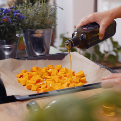 Jemand gießt Bio-Olivenöl über Ofengemüse.