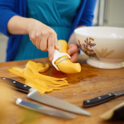 Jemand schält eine gelbe Bio-Rübe mit einem Schäler in Streifen.
