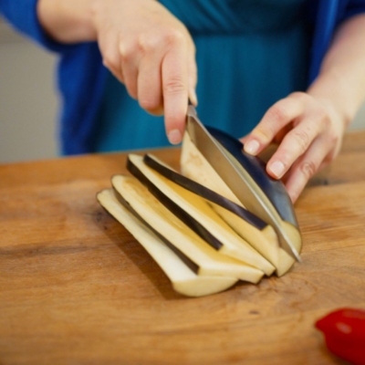 Jemand schneidet eine Bio-Melanzani in Scheiben.