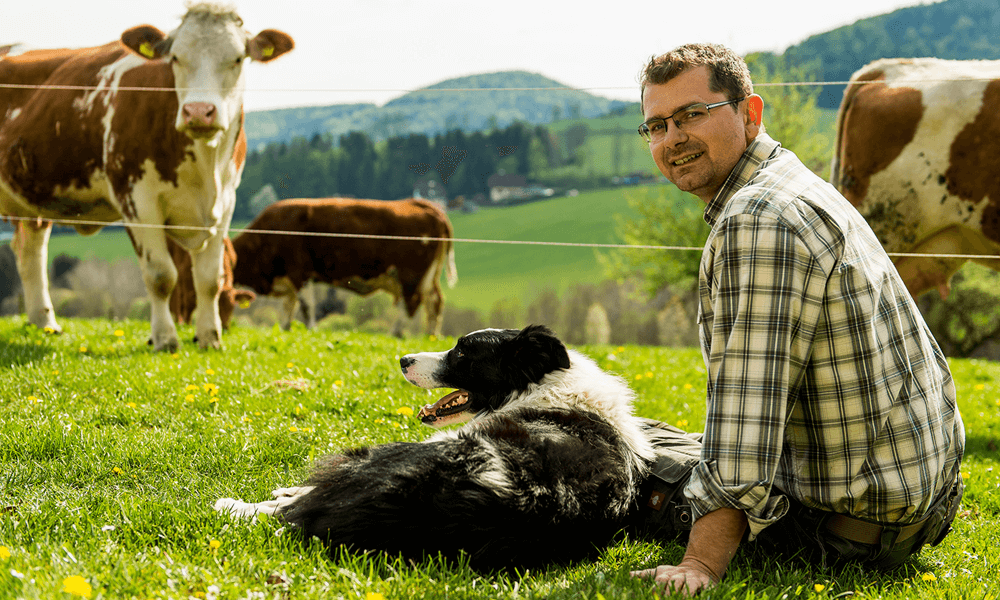 Stefan Eisenberger sitzt mit seinem Hund in der Wiese vor der Weide