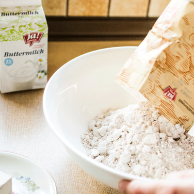 Jemand schüttet eine Packung Ja! Natürlich Bio-Mehl in eine Schüssel.