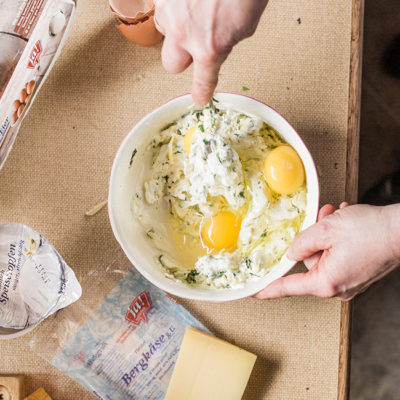Jemand vermengt zwei Bio-Eier mit Speisetopfen und Ja! Natürlich Bergkäse in einer Schüssel.