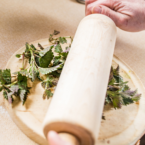 Jemand walkt mit einem Nudelholz über Bio-Brennnesselblätter.