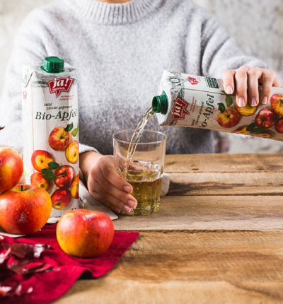 Jemand schenkt Ja! Natürlich Bio-Apfelsaft in ein Glas.