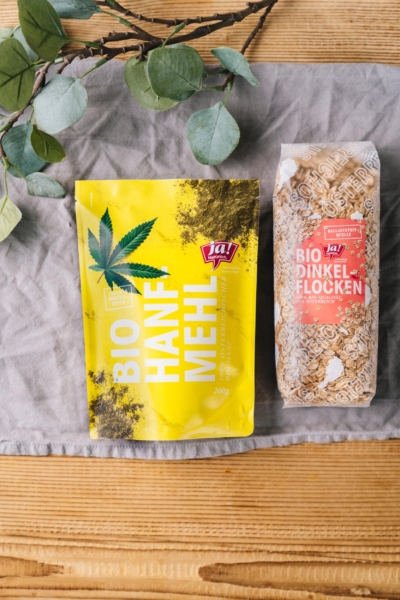 Eine Packung Ja! Natürlich Bio-Hanf Mehl neben einer Packung Dinkel-Flocken.