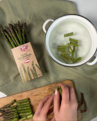 Jemand gibt geschnittenen Ja! Natürlich Bio-Spargel in eine Schüssel.