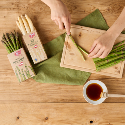 Jemand schneidet Ja! Natürlich Bio-Spargel auf einem Brett.