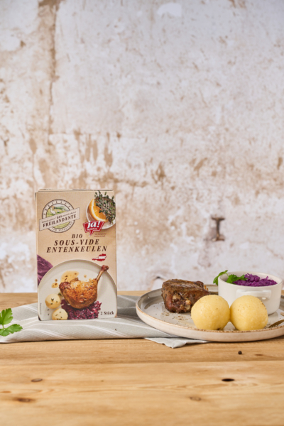 Eine Packung Ja! Natürlich Bio-Sous-Vide Entenkeulen neben einem Entenkeulengericht.