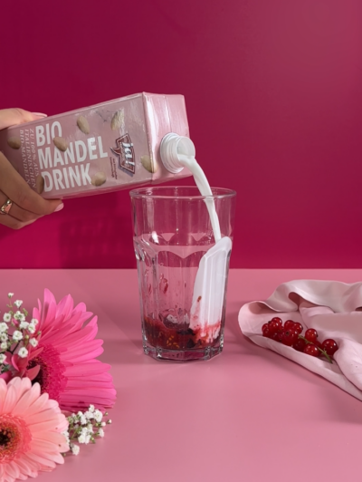 Jemand schüttet Ja! Natürlich Bio-Mandeldrink in ein Glas mit gestampften Beeren.