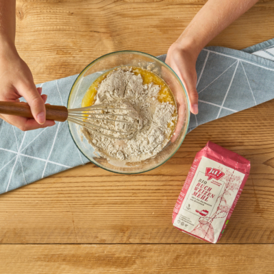 Jemand rührt Ja! Natürlich Bio-Buchweizenmehl und Ei in einer Schüssel.