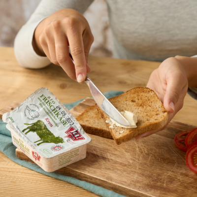 Jemand schmiert Ja! Natürlich Bio-Frischkäse auf ein Brot.