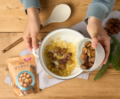 Jemand gibt Ja! Natürlich Bio-Maroni in einen Topf mit angeschwitzten Zwiebeln.