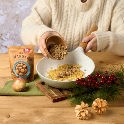 Jemand gibt klein gehackte Ja! Natürlich Bio-Maroni in eine Pfanne mit angeschwitzten Zwiebeln.